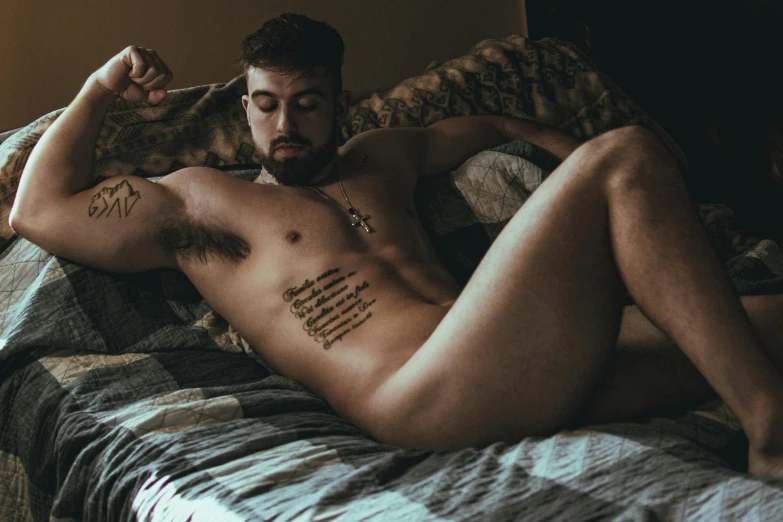 shirtless man sitting in bed showing his chest tattoos