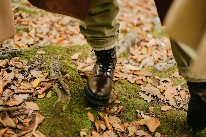 two persons wearing brown boots and green pants in the leaves