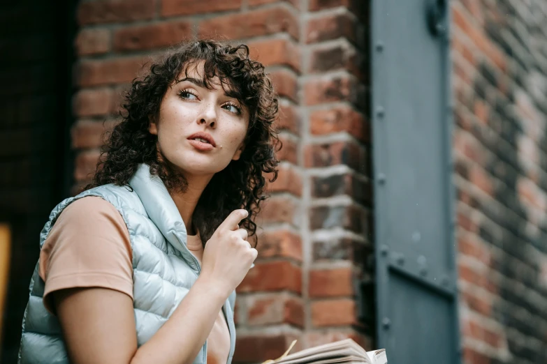 a woman standing by a brick wall and looking up