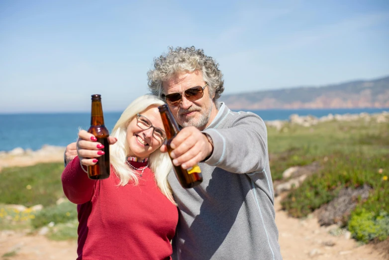 a man and woman are sharing beer near the ocean