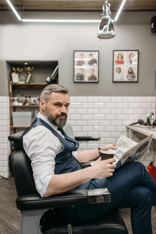 a man sitting on a barber chair and reading a paper