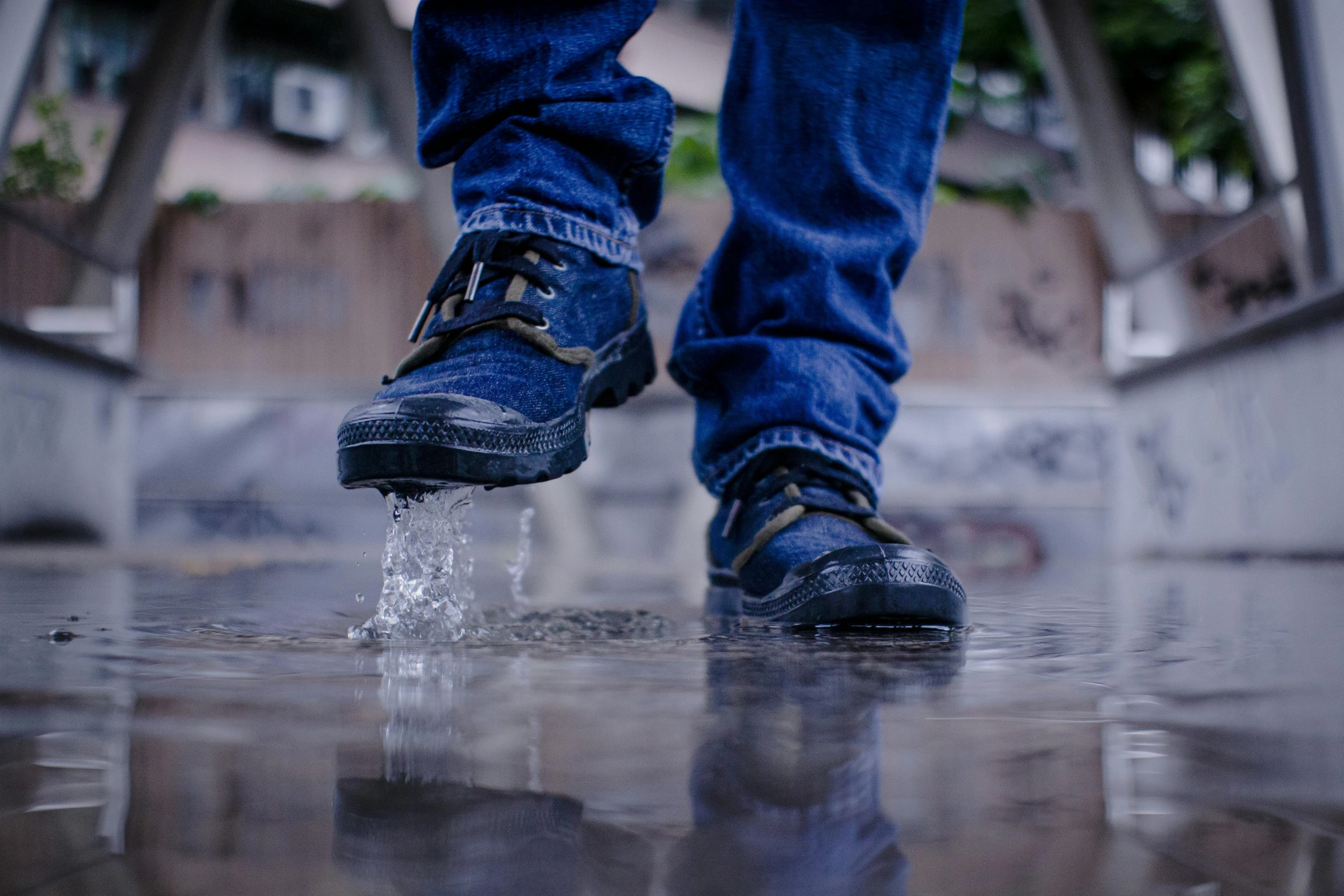 man in sneakers walking over an opening with water splashing out of his shoe