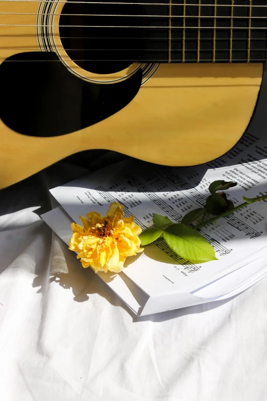 a sheet of music sits next to a guitar and yellow rose