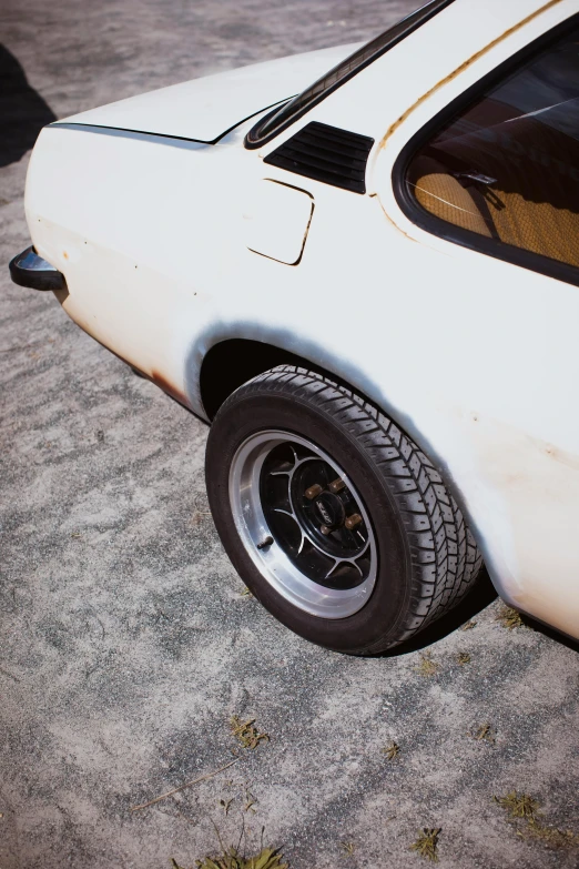 the front wheel and fender of a white mustang with a black fender and an antenna, with a worn rim