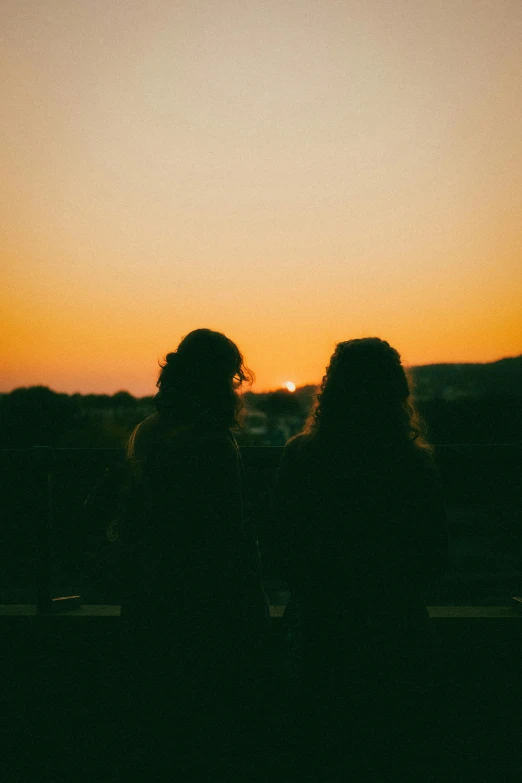 two woman standing in front of a sunset