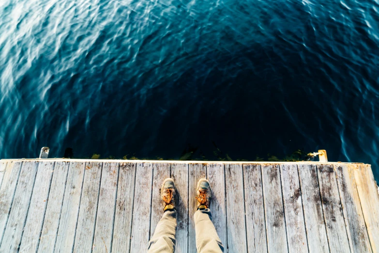 feet hanging off the side of wooden planks on water