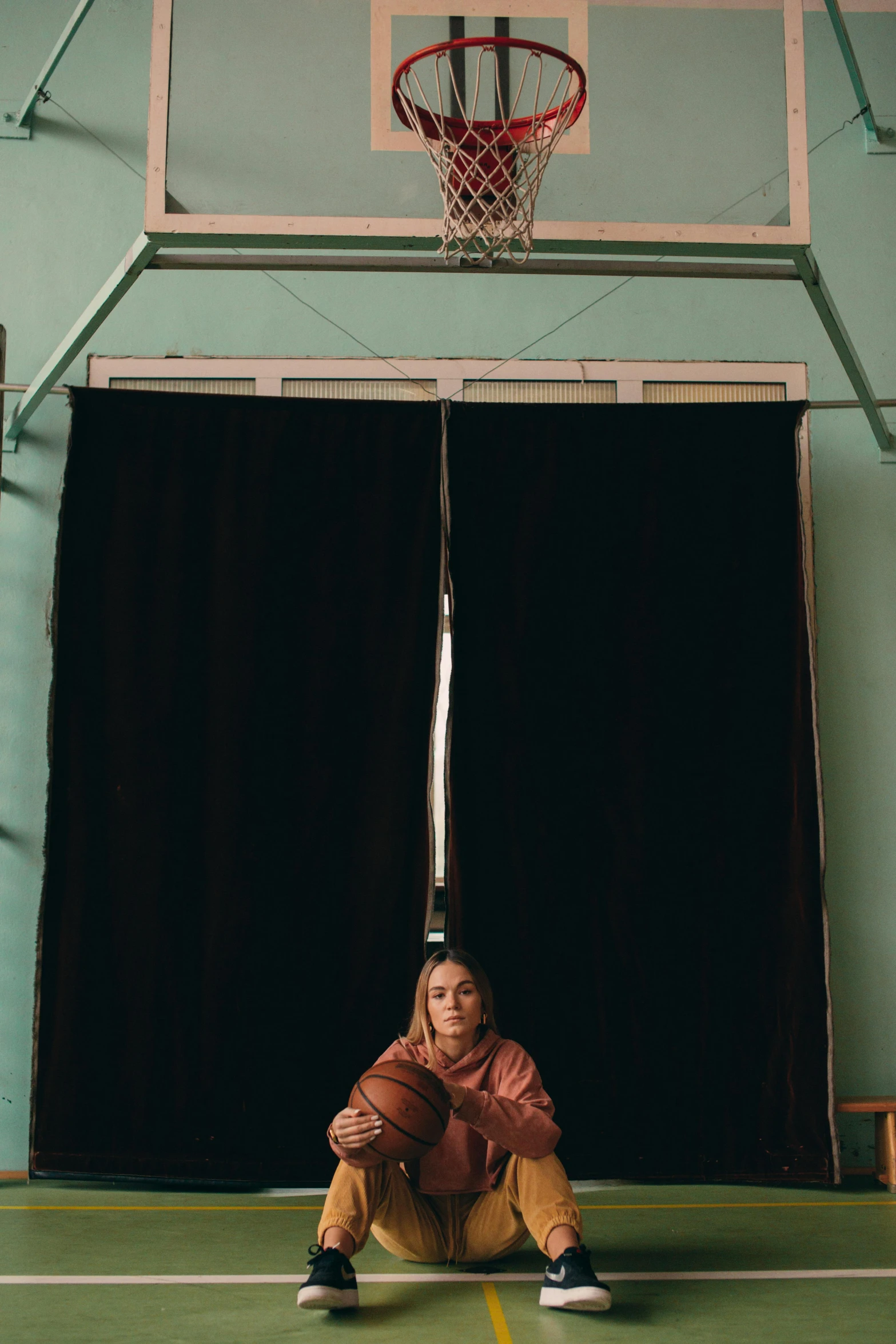 a woman squatted on the floor in front of a basketball net