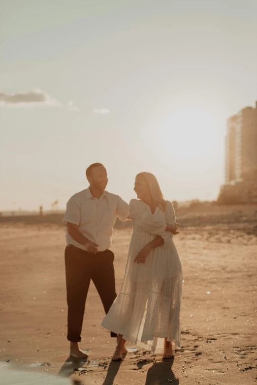 a couple stands on the beach at sunset