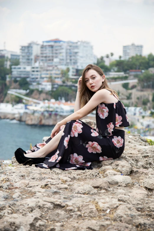 the young woman is sitting on the rocks near the water