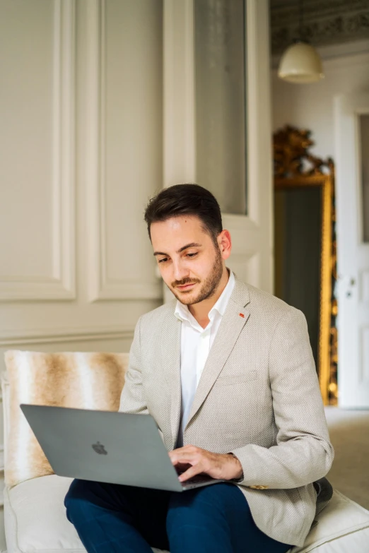 a man sitting on a white couch using a laptop computer