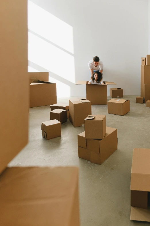 a man sits on an open cardboard box surrounded by boxes