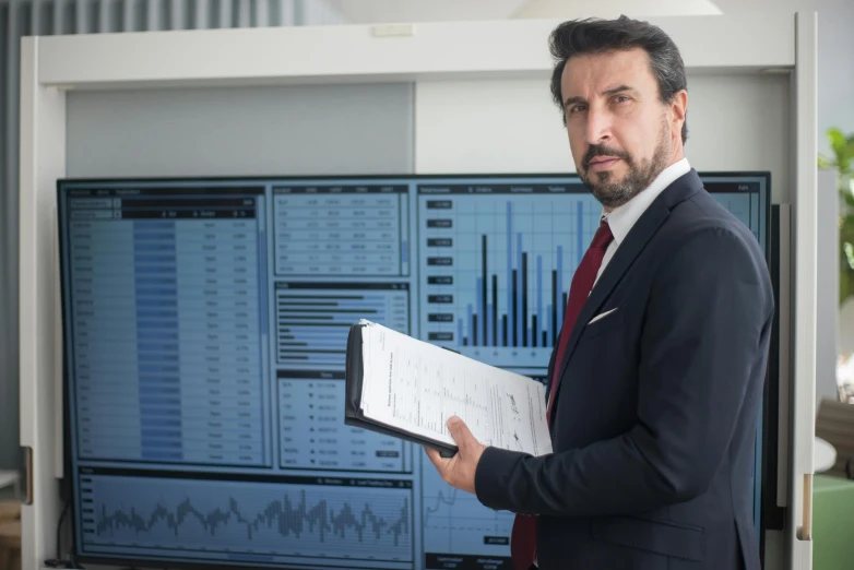 a man holding up some paperwork in front of a screen