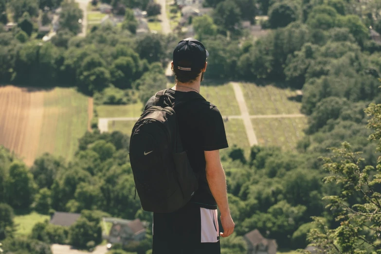 the man wearing a back pack stands on top of a hill looking over a countryside