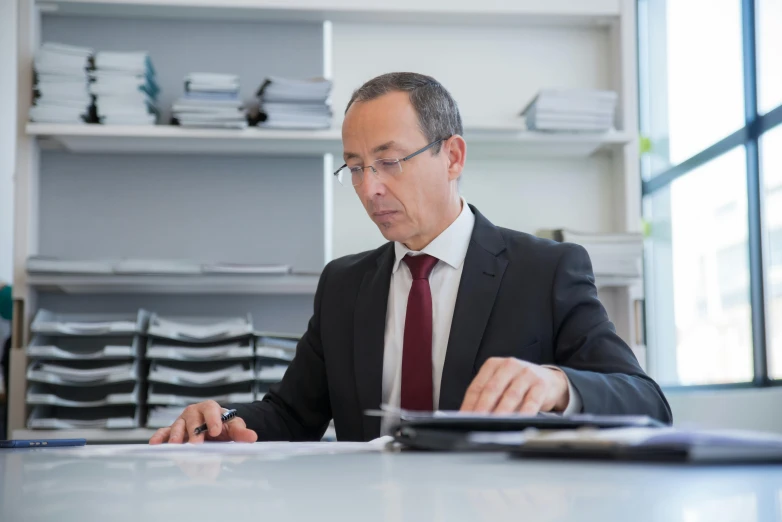 the man in the suit is sitting at a desk working on his laptop