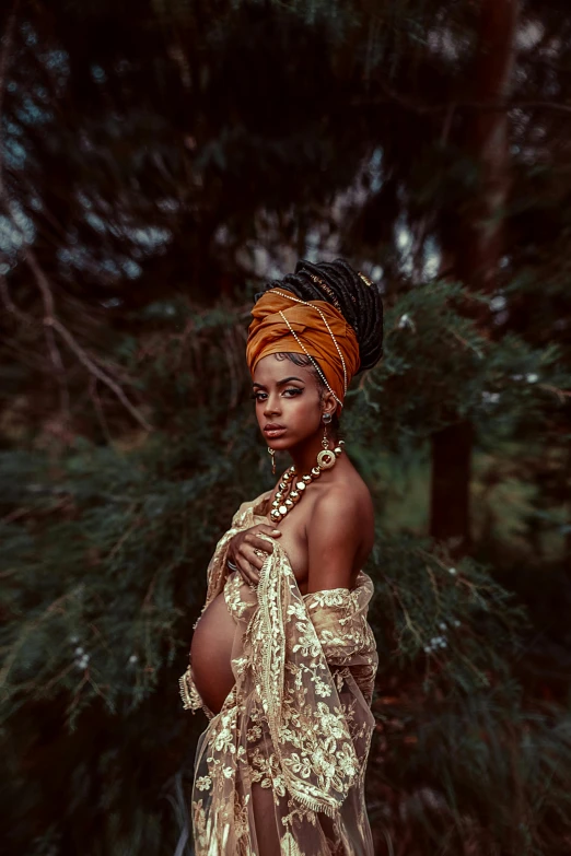 a woman wearing a gold dress in front of some trees