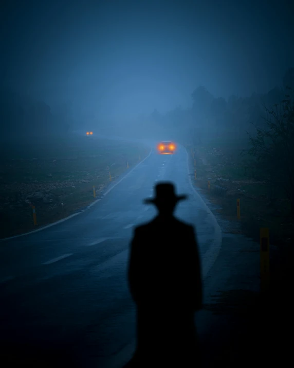 the silhouette of a man in a hat standing next to a road