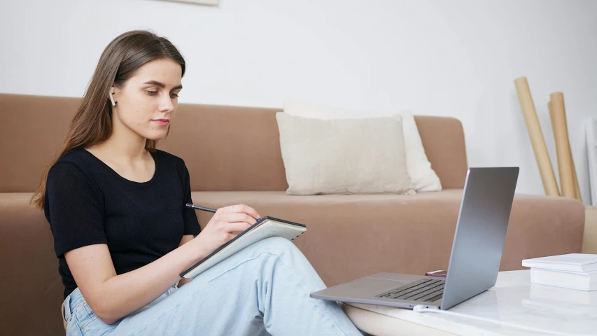 a woman is sitting on a couch with a laptop and notebook