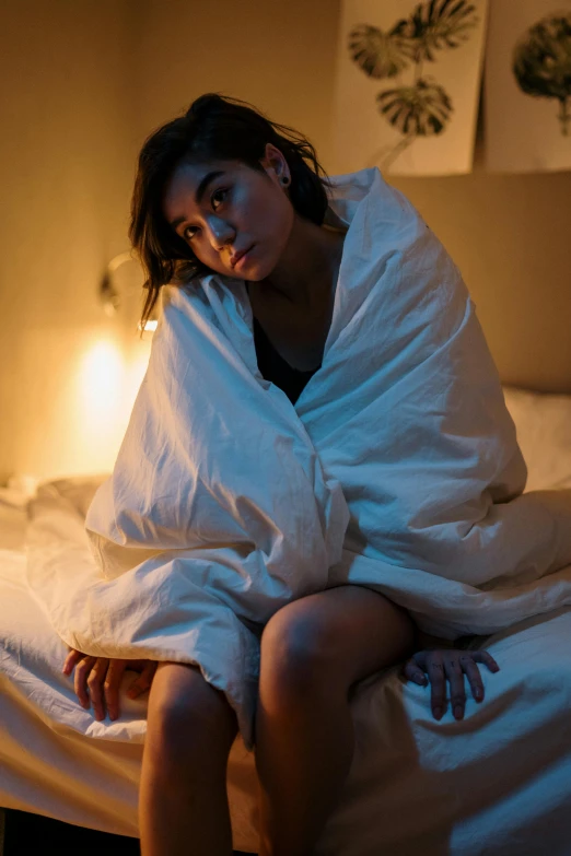 a woman sitting on her bed wrapped up in blankets