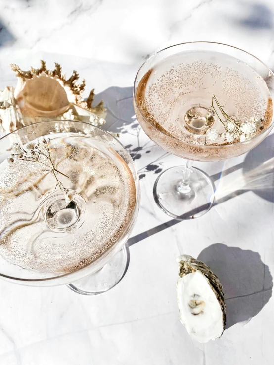 two wine glasses with gold glitter and silver rims sitting on a table with other wine glasses, on the table are shells