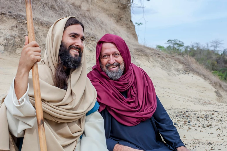 two people sitting on a sandy ground with sticks