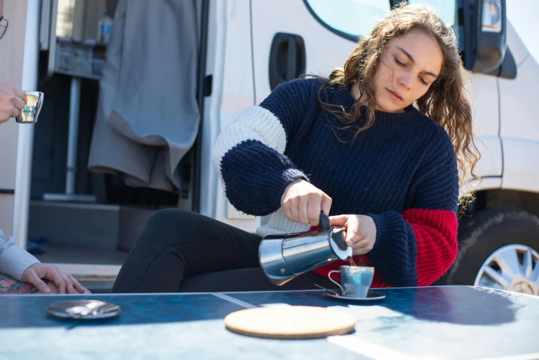 a woman sitting on the ground pours tea from a mug