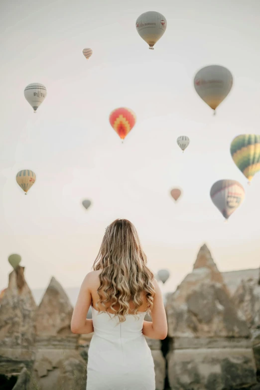 a beautiful woman in a wedding gown standing looking out at  air balloons