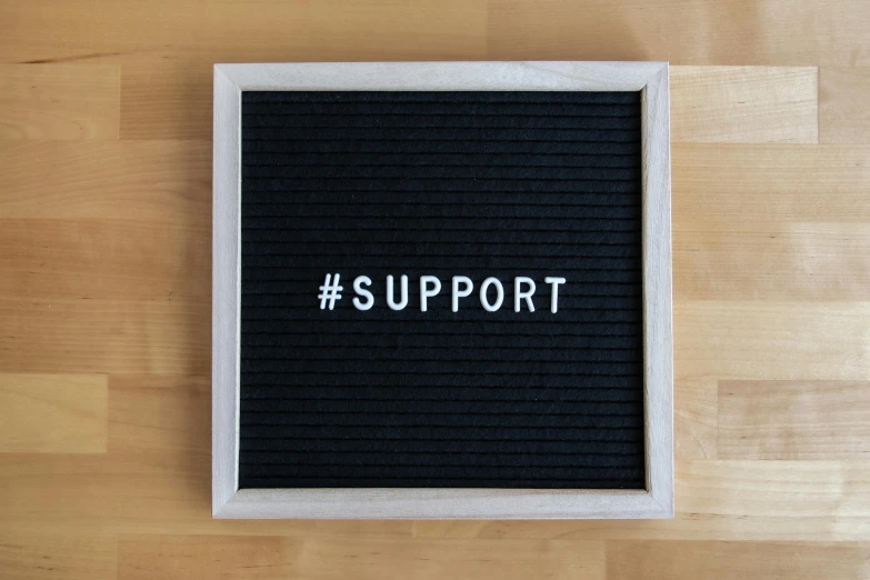 black framed picture on a wooden floor that reads support