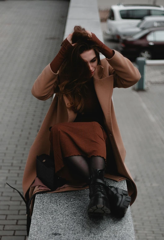 a woman sitting on a concrete ledge wearing a jacket and skirt