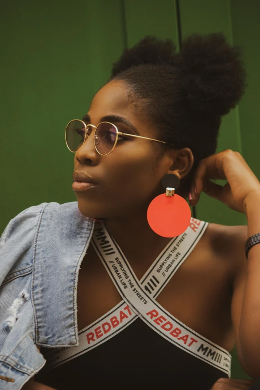 a woman wearing a jean jacket, with a ribbon around her neck and pair of round gold - colored sunglasses