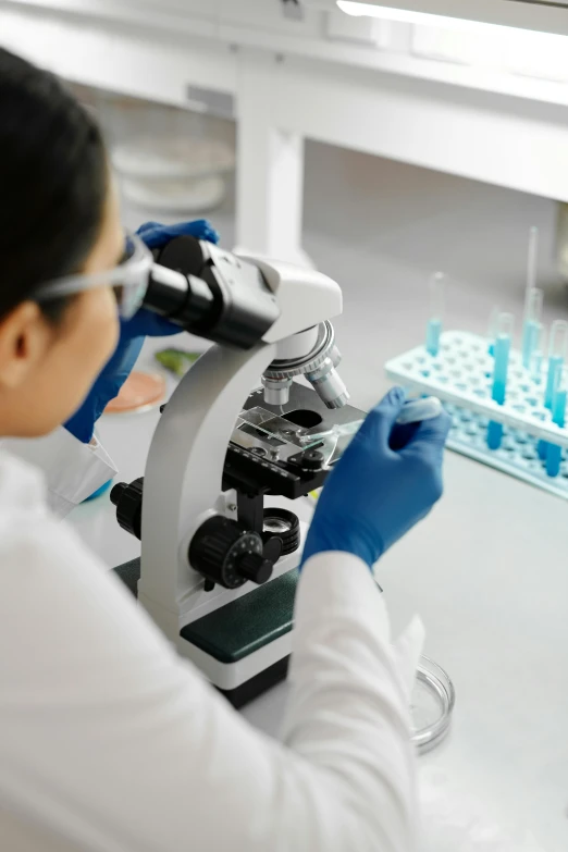 female student in white shirt using microscope in lab