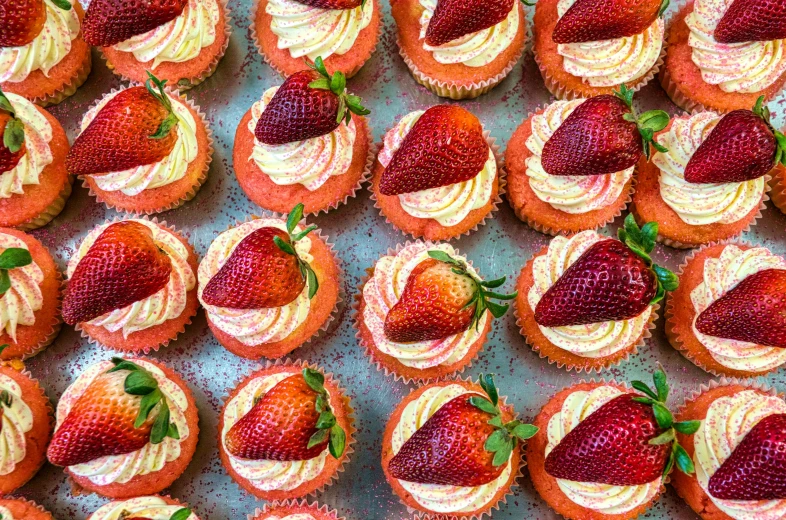 some cupcakes with strawberries on them sit together