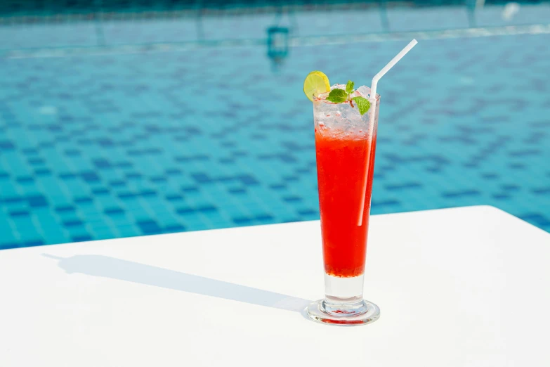 a drink garnished with lime on a table near a swimming pool