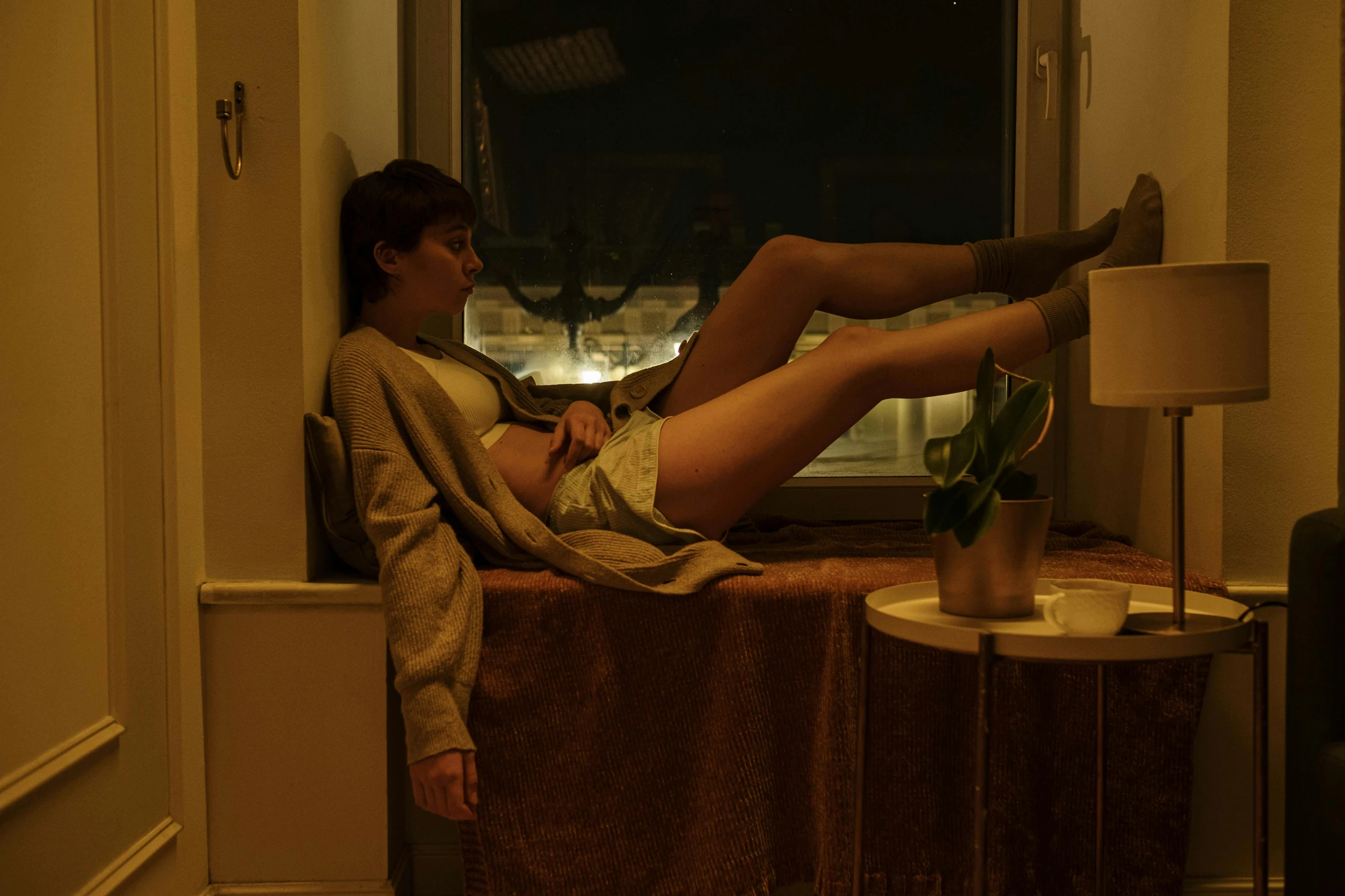 a young man sitting in a window sill looking out the window