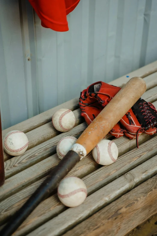 baseballs and bats sit atop a wooden bench