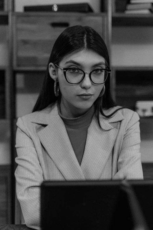 a woman in a business suit and glasses working on a laptop