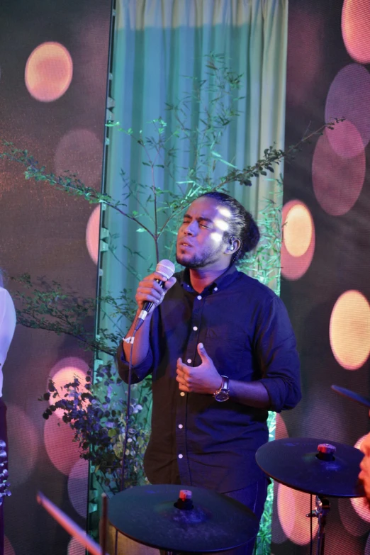 a man holding a microphone while standing next to a tree