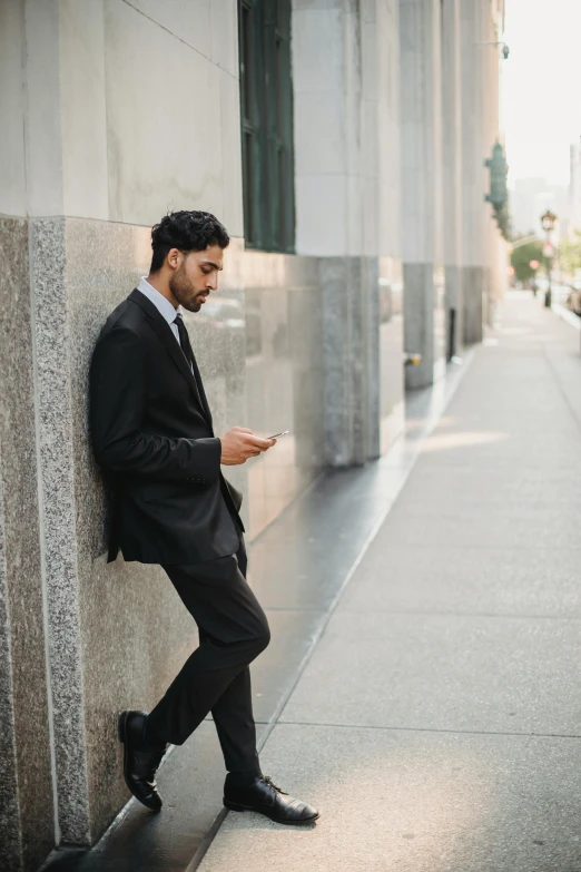 a man wearing a suit leaning against a wall