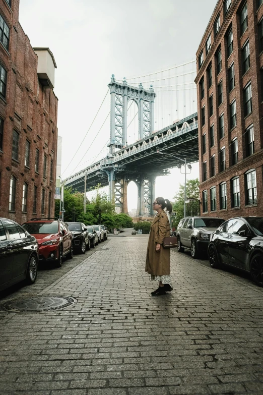 a woman standing on the sidewalk in front of a bridge