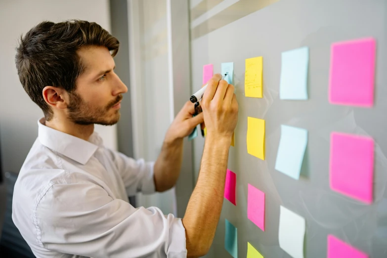 man doing a post - it with colorful notes on a whiteboard