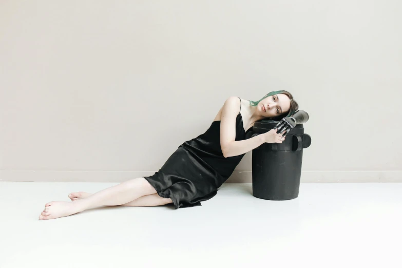 a woman wearing a black dress and head scarf sits beside a trash can in the studio