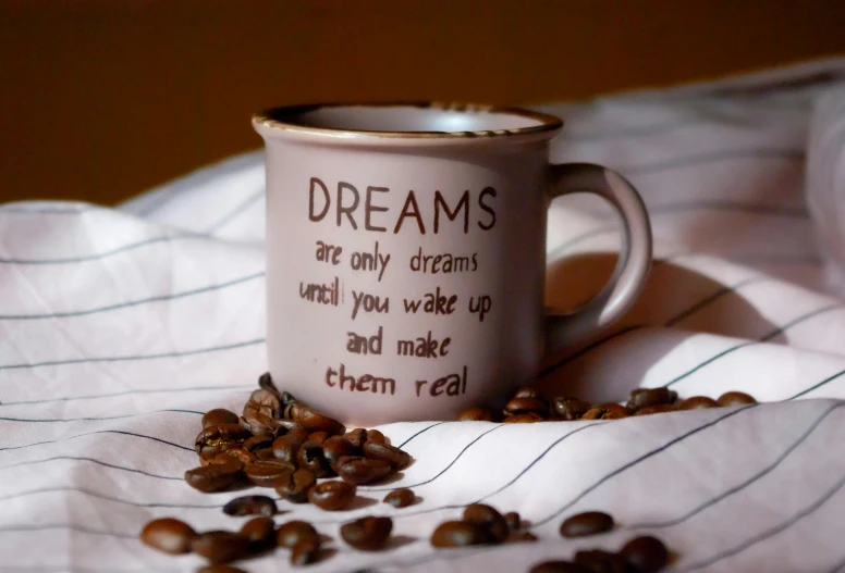 a white cup on a bed with coffee beans