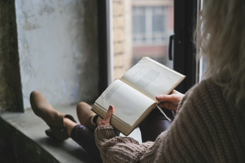 the woman is reading a book near a window