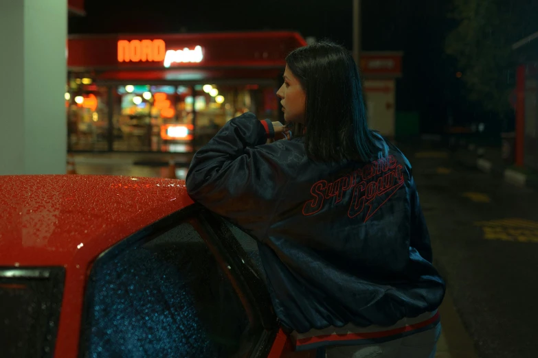 a girl leans on the back of an orange car at night