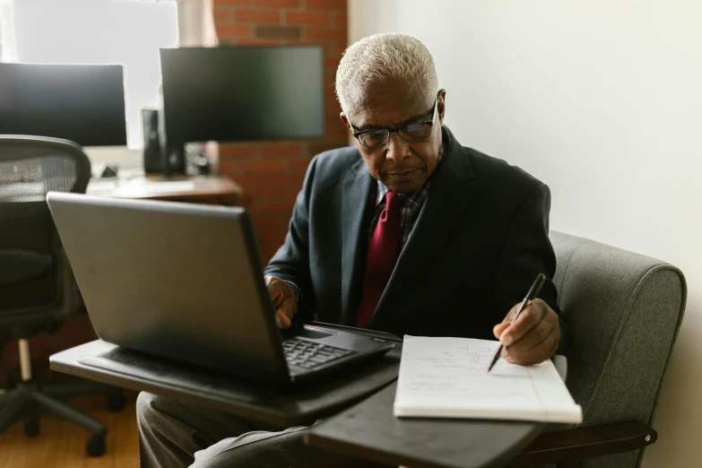 the man is writing on his notepad next to his laptop