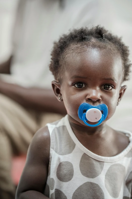 an african girl with blue pacifier on her nose