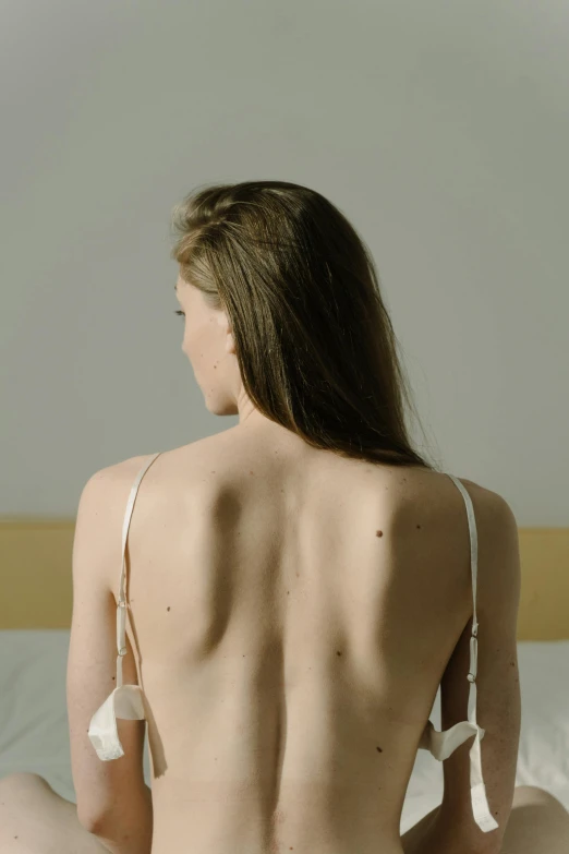 back view of a woman with long, brown hair and no  wearing lingerie sitting in bed