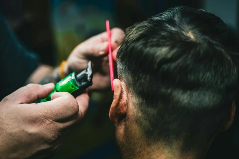 the man is  another man's hair while holding a green toothbrush