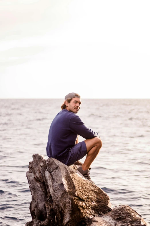 a man sitting on top of a rock on top of the ocean