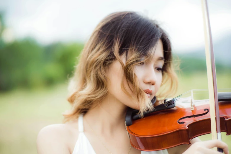 a woman playing the violin outside while wearing a white top