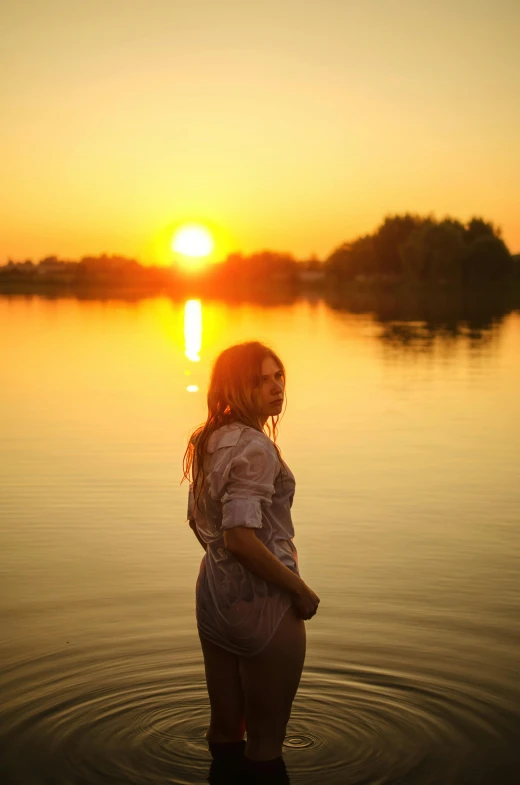 a woman stands in the water while sunset shines over the lake